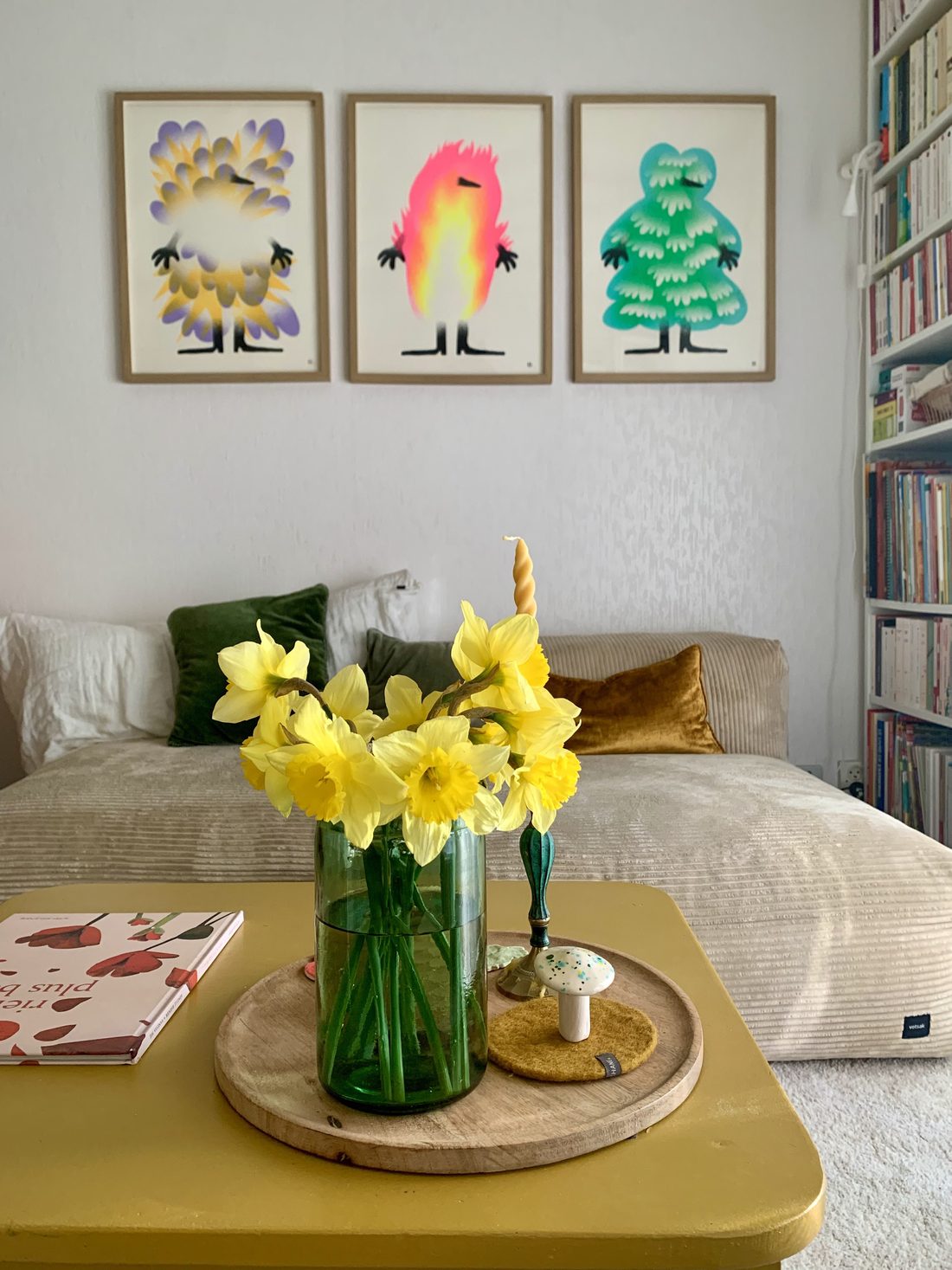 Le séjour aménagé : canapé clair, table basse jaune, affiches encadrées, bibliothèque garnie